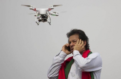 Pakistan&#039;s cricketer-turned-politician Imran Khan talks over a phone as a camera-equipped drone hovers outside a parliament in Islamabad on Thursday.